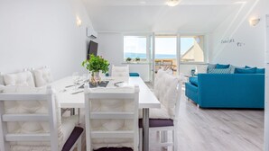 A modern living space with a dining area, a sofa, and a view of the sea.
