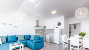 A modern living room with a blue sofa, a dining table with chairs, and a kitchen area in the background.