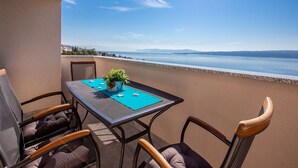 A balcony with a table and chairs overlooking a calm sea and distant mountains.