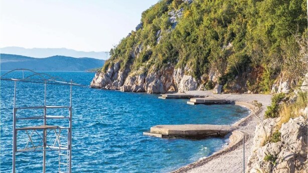 A coastal area with a rocky shoreline, a metal structure, and a clear blue sea.