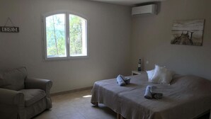 A bedroom with a bed, a chair, a window, an air conditioner, and a painting on the wall.