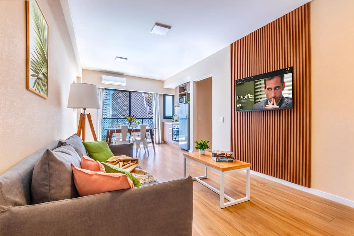 Uma sala de estar moderna com um sofá, uma mesa de centro e uma TV fixada numa parede de madeira.