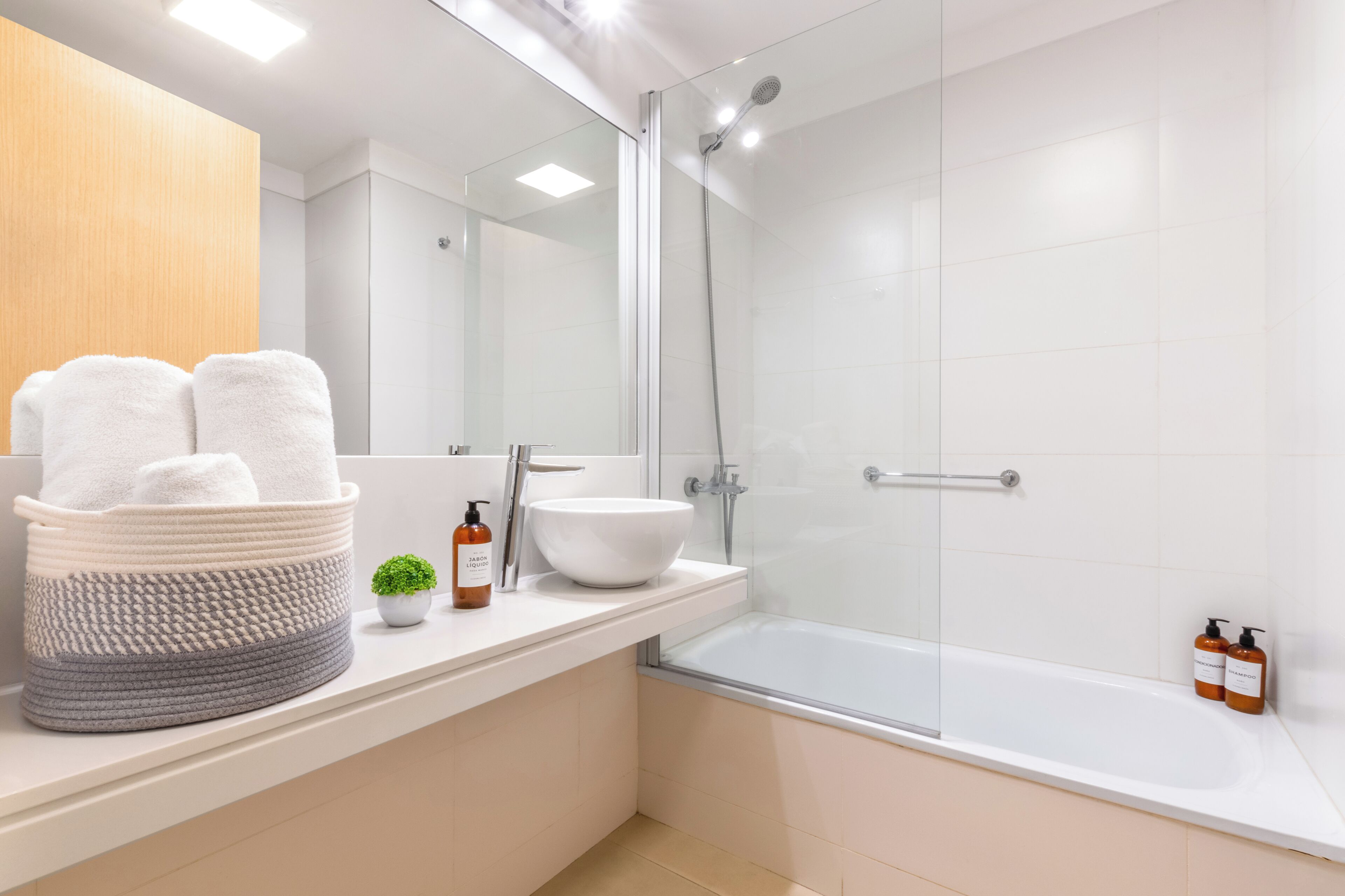 Ein modernes Badezimmer mit Duschkabine aus Glas, einer weißen Badewanne und einem Waschbecken mit großer Schüssel. Auf der Ablage befinden sich zwei Shampooflaschen.