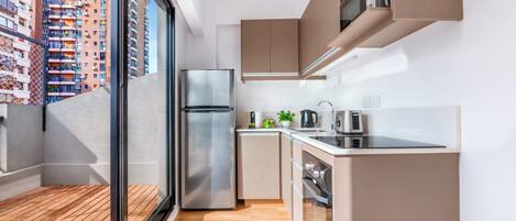 A modern kitchen with a stainless steel refrigerator, a small countertop, and a view of a cityscape through a large window.