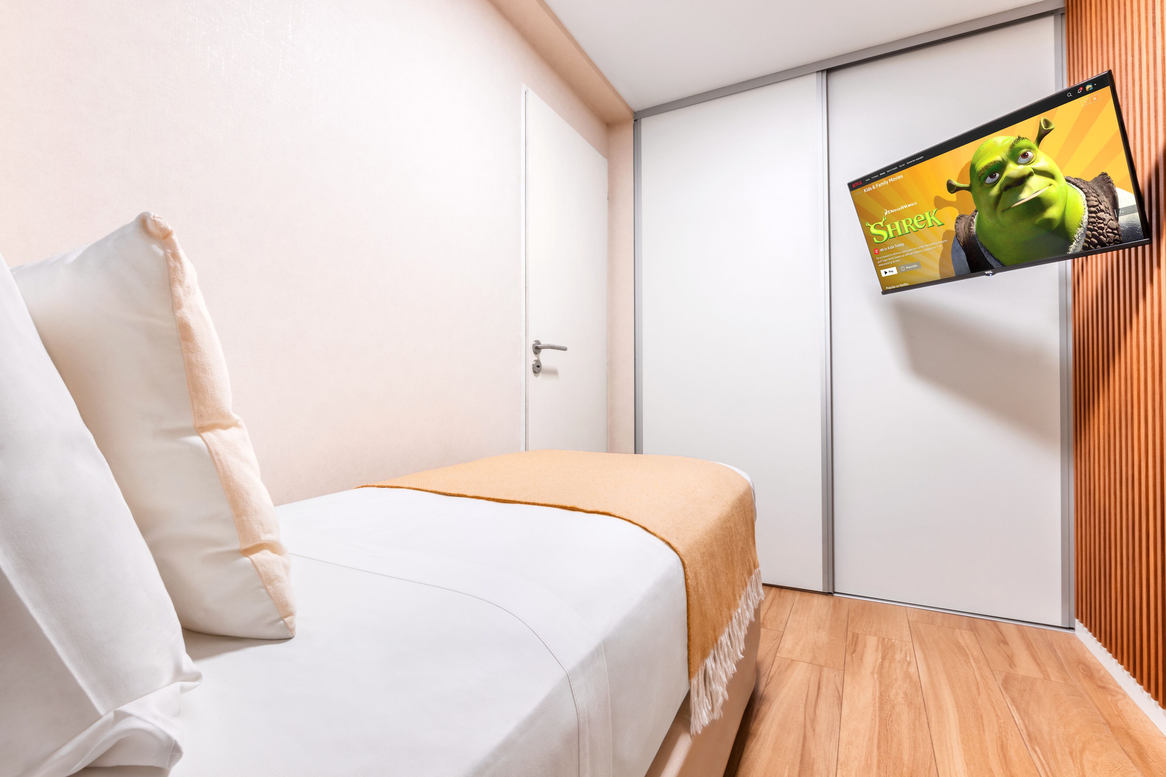 Une chambre d’hôtel avec un lit, un téléviseur fixé au mur et un plancher en bois.