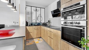 A modern kitchen with wooden cabinets, a built-in oven, and pendant lighting. - Beautiful And Spacious Apt At 19 Min From Downtown (Toulouse)