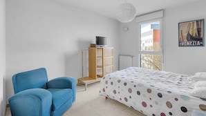 A bedroom with a bed, a blue chair, a wooden wardrobe, and a window with a view of buildings. - Beautiful And Spacious Apt At 19 Min From Downtown (Toulouse)