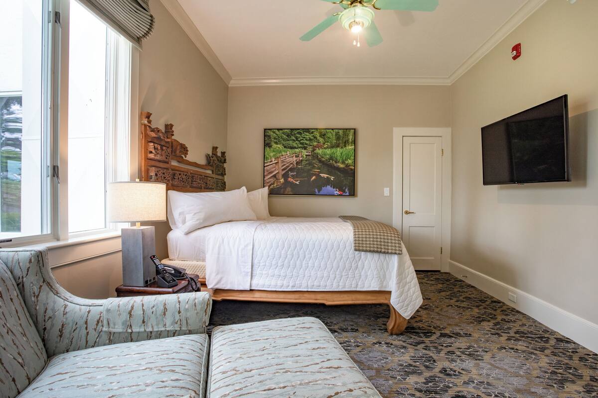 Habitación de hotel con una cama, una silla, una lámpara, un televisor y un cuadro en la pared.