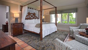 A four-poster bed with a canopy, a wooden nightstand, a chair, and a view of greenery through large windows. - Shangri-La Springs (Bonita Springs)