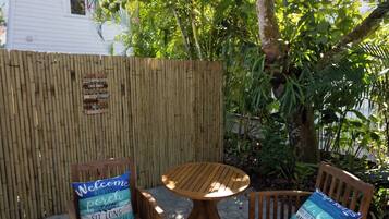 Un espacio al aire libre con sillas de madera y una mesa redonda, rodeado por una valla de bambú y abundante vegetación.