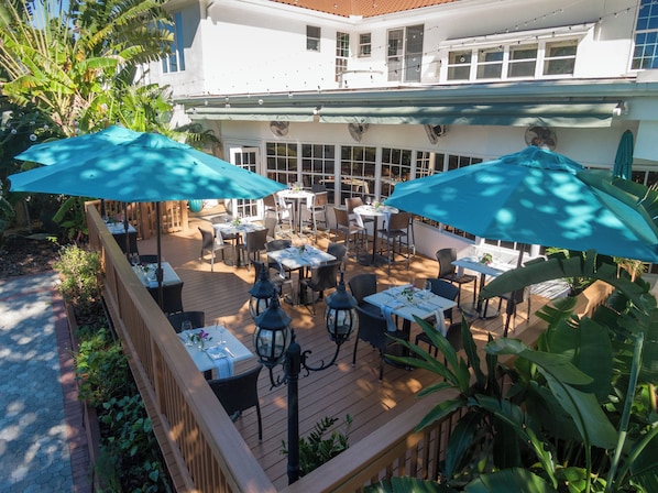 An outdoor patio with tables and chairs, surrounded by greenery and umbrellas.