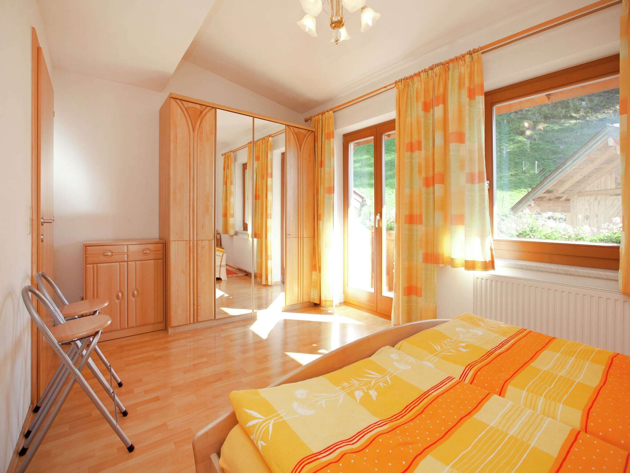 Un dormitorio con cama, una silla, un armario y un ventanal con cortinas.