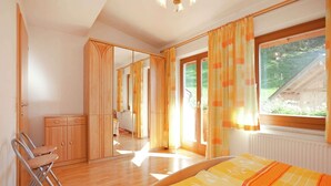 Um quarto com cama, uma cadeira, um guarda-roupa e uma janela com cortinas.