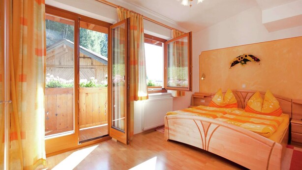 Quarto com cama de madeira, uma janela grande e vista para um deck de madeira.