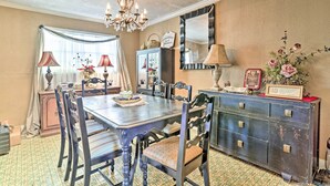 Een eetkamer met een houten tafel, stoelen, een kroonluchter en een kast met decoratieve objecten.