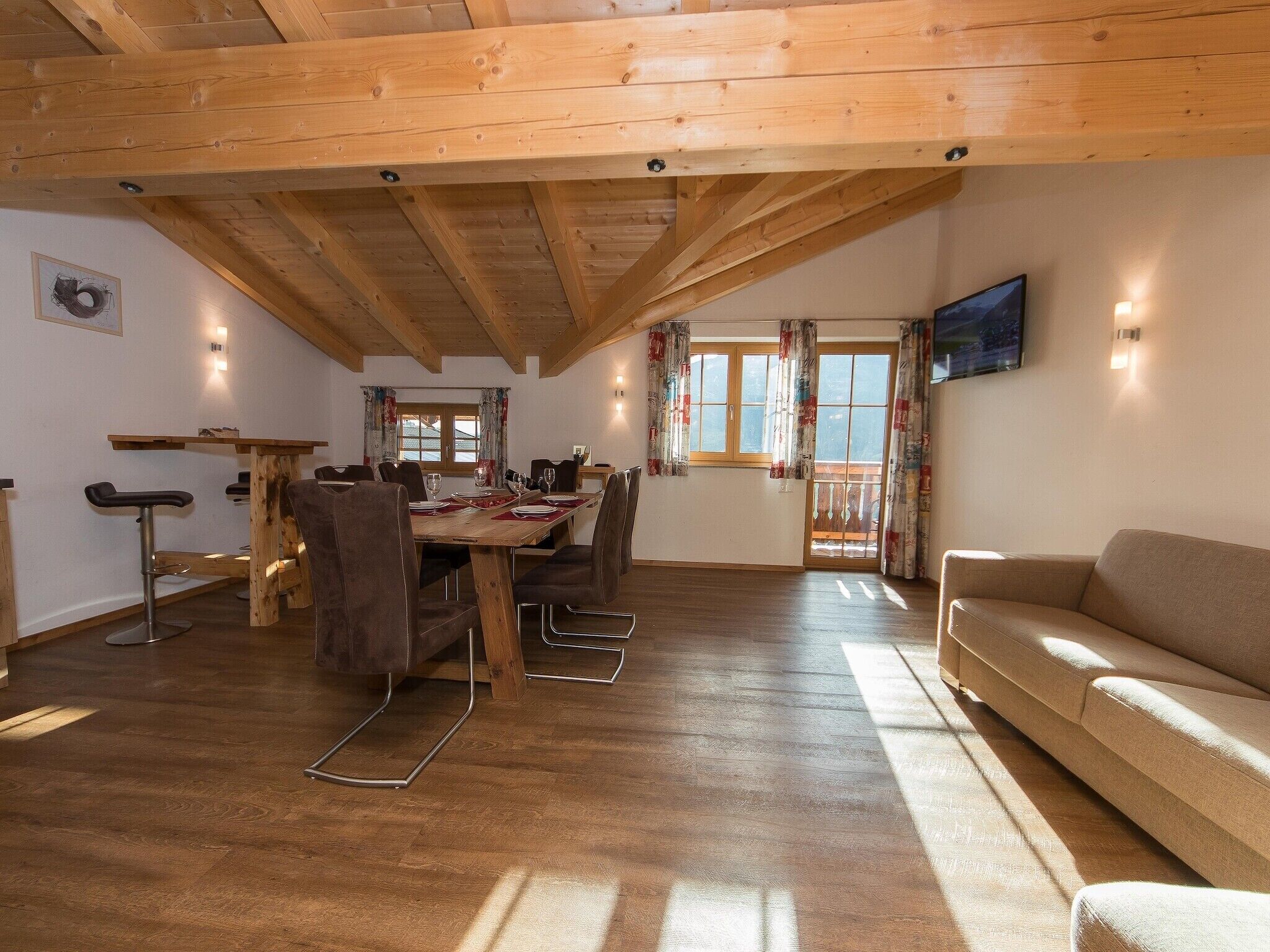 Un coin repas avec une table et des chaises en bois, un canapé et un téléviseur fixé au mur.