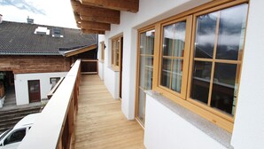 A narrow balcony with wooden beams, large windows, and a view of neighboring buildings and mountains. - Apartment in Kaprun near the ski area (Kaprun)