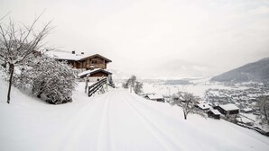 A wooden chalet with a snow-covered roof, a wooden fence, and a snow-covered path leading to a village. - Apartment in Kaprun near the ski area (Kaprun)