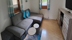 A modern living room with a grey sofa, two round side tables, a wooden cabinet, and a TV on a wooden stand. - Apartment in Niedernsill near Ski Slopes (Niedernsill)