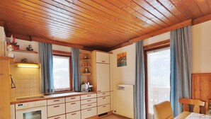 A kitchen with wooden cabinets, a built-in oven, and a dining area with a table and chairs. - Apartment in Niedernsill near Ski Slopes (Niedernsill)