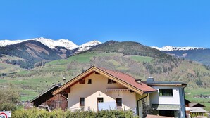 A traditional chalet with a sloped roof, a small balcony, and a view of snow-capped mountains. - Apartment in Niedernsill near Ski Slopes (Niedernsill)