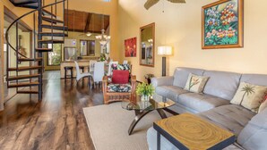 A spacious living area with a wooden staircase, a ceiling fan, a dining area, and a large painting on the wall. - KKSR#8301 AMAZING 3 BEDR, TOP FLOOR CORNER UNIT: REMODELED, AIR CONDITIONING (Kailua Kona)
