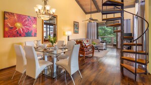 A spacious living area with a dining table, chairs, a sofa, a coffee table, a chandelier, a large painting, a spiral staircase, and a ceiling fan. - KKSR#8301 AMAZING 3 BEDR, TOP FLOOR CORNER UNIT: REMODELED, AIR CONDITIONING (Kailua Kona)
