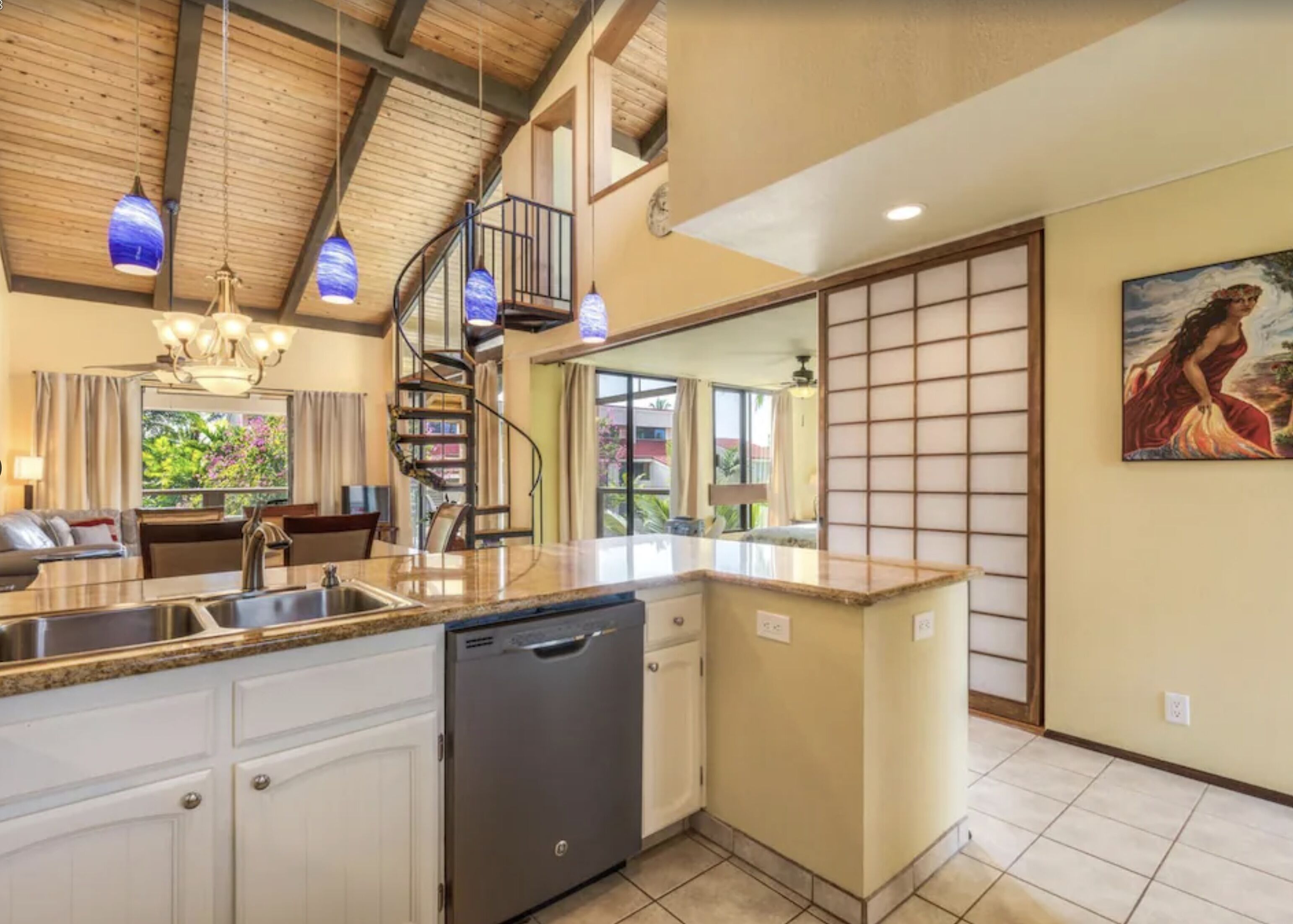 A kitchen with a central island, a dishwasher, and a spiral staircase.