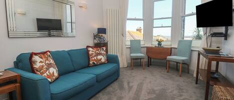 A living room with a sofa, chairs, a TV, and a view of buildings.