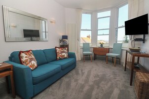Una sala de estar con un sofá, sillas, un televisor y vistas a edificios.
