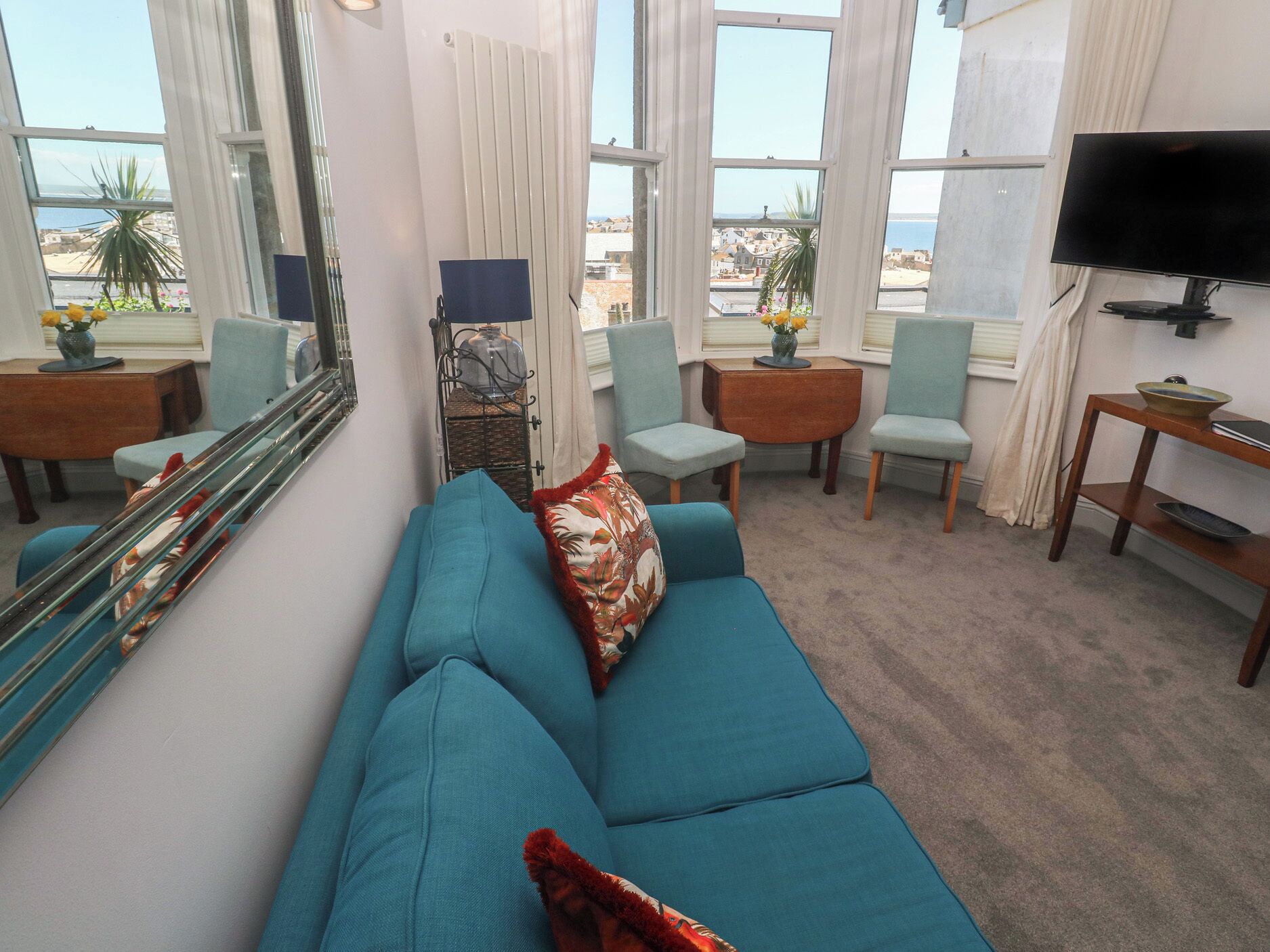 A living room with a blue sofa, two chairs, a TV, and large windows with a view.