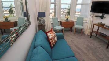 A living room with a blue sofa, two chairs, a TV, and large windows with a view.