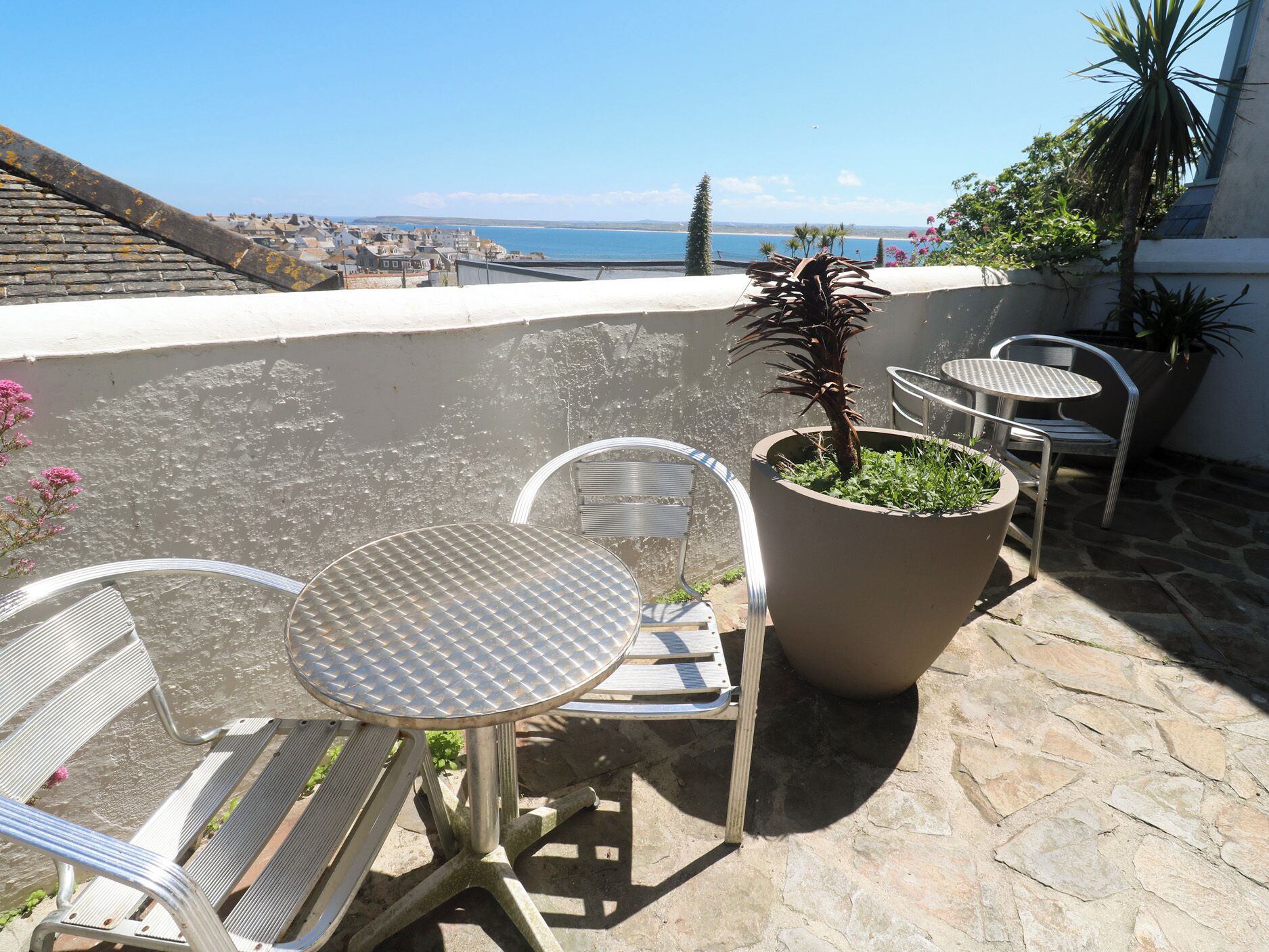 A terrace with metal chairs and a table, a potted plant, and a view of the sea.