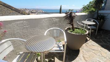 Una terraza con sillas de metal y una mesa, una planta en maceta y vistas al mar.