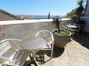 A terrace with metal chairs and a table, a potted plant, and a view of the sea. - Heron (St Ives)