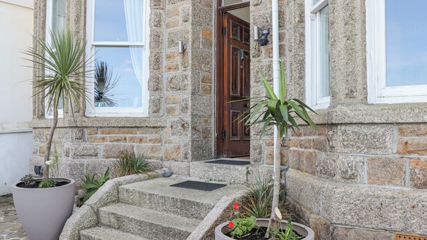 Un edificio de piedra con una escalera de piedra que lleva a una puerta de madera. Hay plantas en macetas en la escalera y alrededor del edificio.