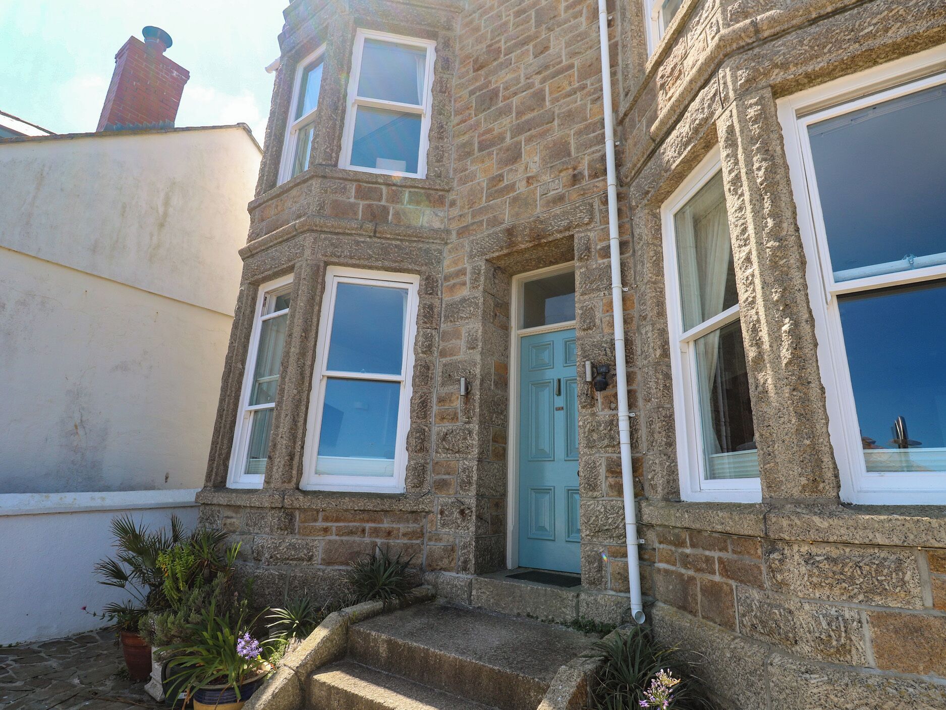 A stone building with a blue door, multiple windows, and a small garden area with potted plants.