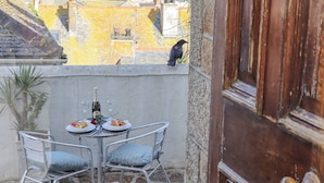 Un balcón con una mesa dispuesta para dos, una botella de vino y platos de comida.