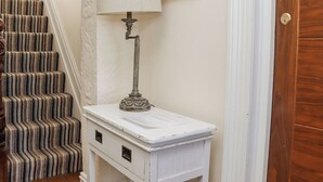 Una escalera con alfombra a rayas, una mesa blanca con cajones, una lámpara y una puerta con cerradura.