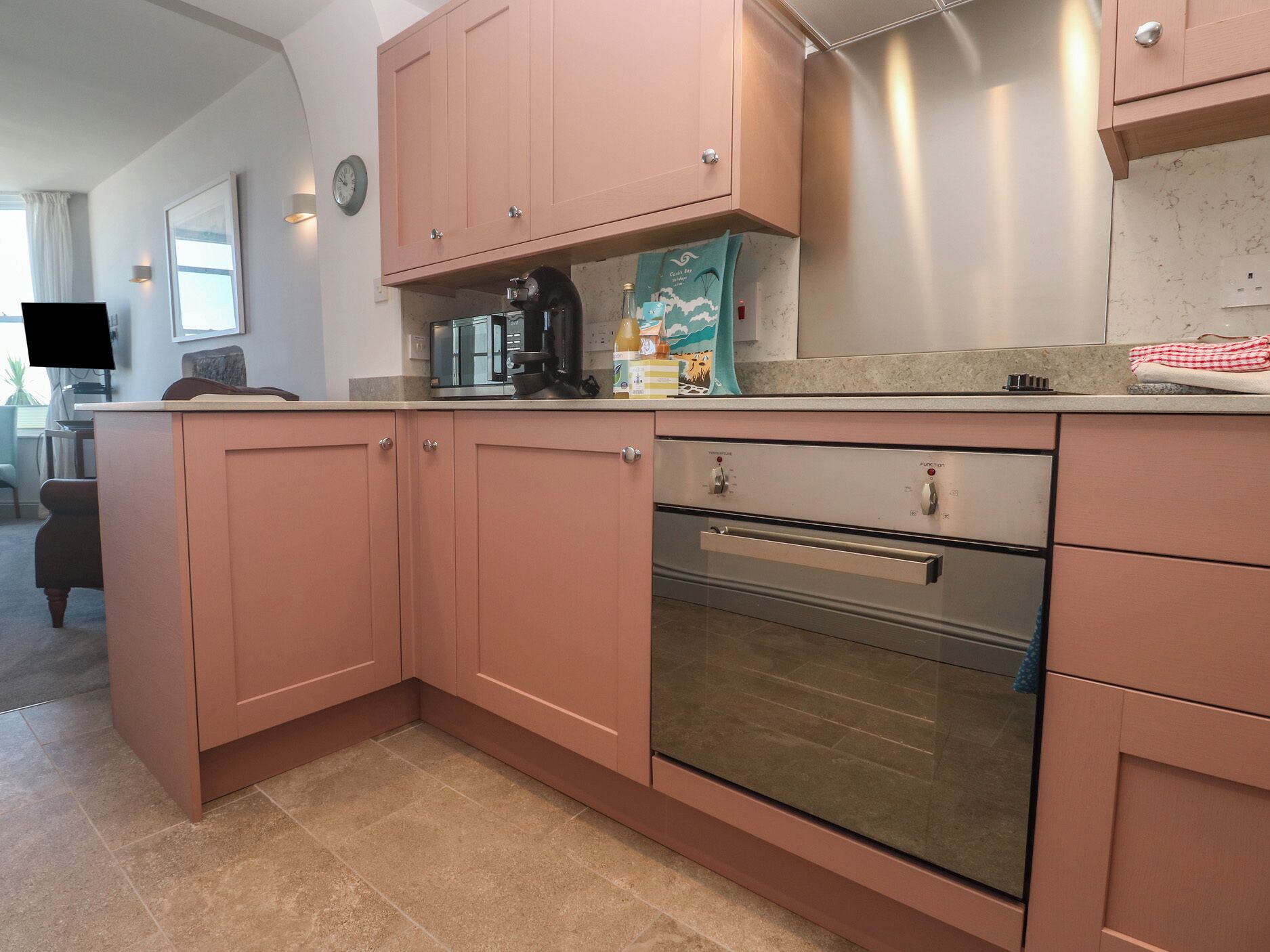 Una cocina con armarios rosados, una cafetera, un tostador y un refrigerador.