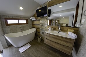 Une salle de bain moderne avec une baignoire sur pieds, un meuble-lavabo avec un miroir et un téléviseur fixé au mur.