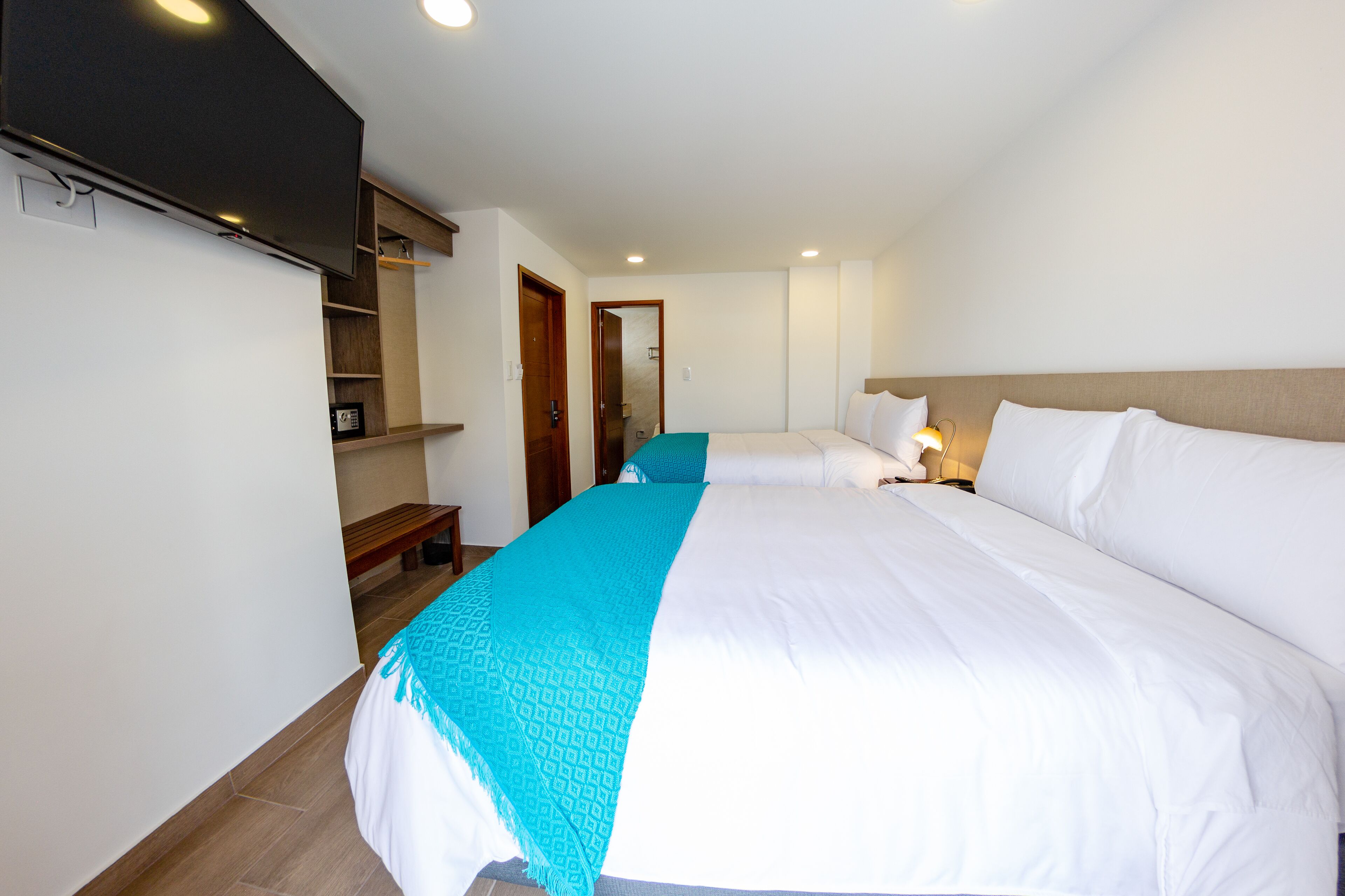 Una habitación de hotel con una cama grande, un televisor montado en la pared, un banco de madera y un espejo.