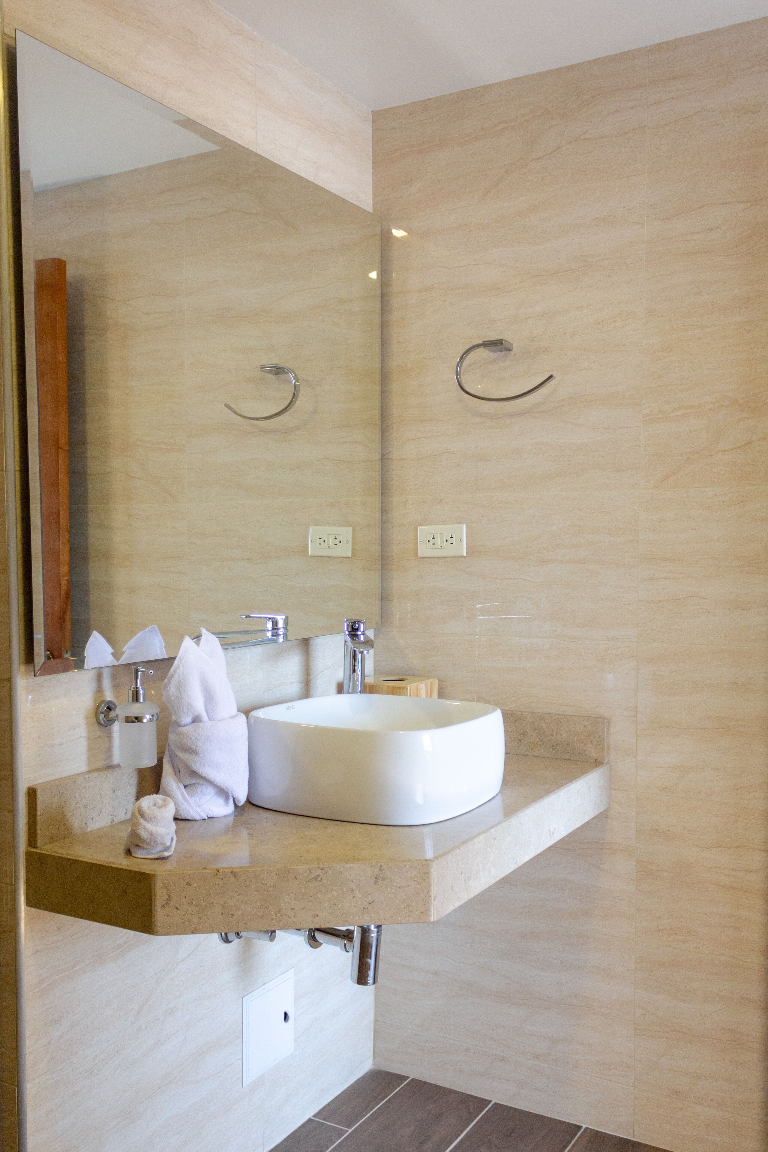 Un baño moderno con un espejo grande, un lavabo redondo y un perchero para toallas.