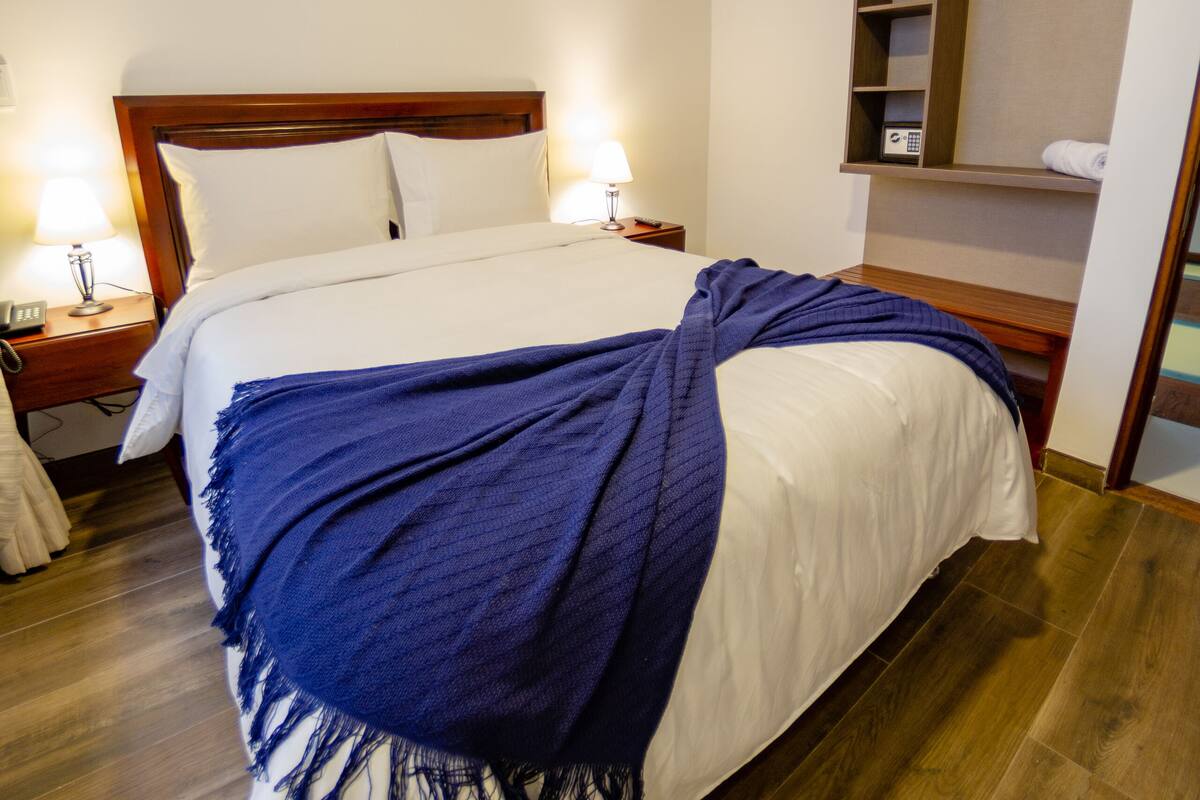 A neatly made bed with a white and blue blanket, wooden headboard, bedside lamps, and a wooden nightstand.