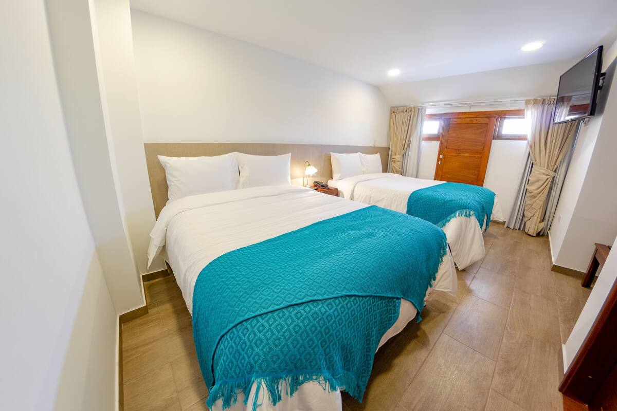 A hotel room with two beds, a TV mounted on the wall, and a wooden door.