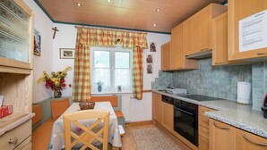 A compact kitchen with wooden cabinets, a built-in oven, and a window with curtains. - Apartment Kitzbuhel near Ski Slopes (Kitzbühel)