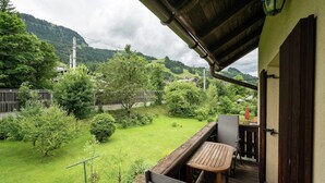 A balcony with a table and chairs, overlooking a well-maintained garden and a mountainous landscape. - Apartment Kitzbuhel near Ski Slopes (Kitzbühel)
