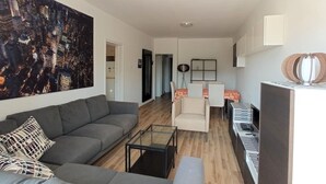 A modern living room with a grey sofa, a glass coffee table, and a large abstract painting. - Umm Haram whole apartment · 5 min walk to the Beach! NETFLIX & fast Internet (Larnaca)