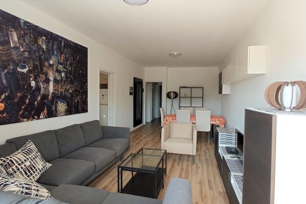 A modern living room with a grey sofa, a glass coffee table, and a large abstract painting.