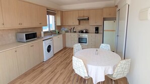 A compact kitchen with wooden cabinets, a washing machine, a microwave, a stove, and a refrigerator. - Umm Haram whole apartment · 5 min walk to the Beach! NETFLIX & fast Internet (Larnaca)
